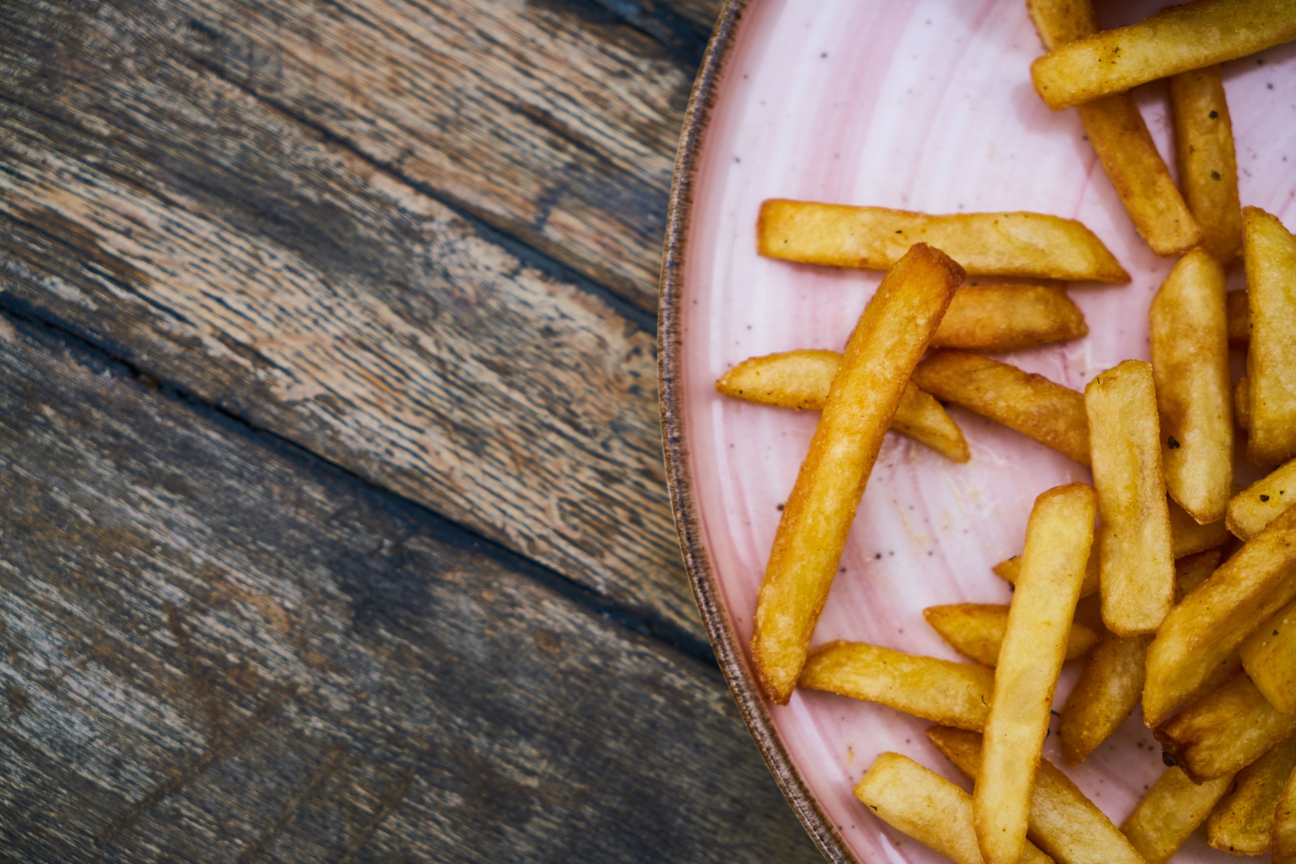 Close-up of golden french fries on a pink plate over a rustic wooden table background.
